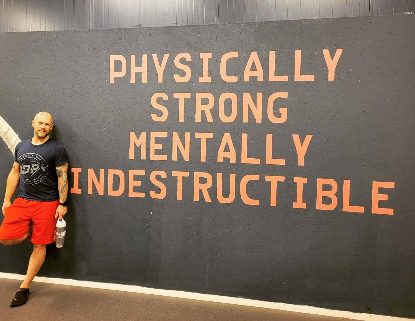 Paal Erik står ved en vegg der det står: Physically strong mentally indestructable.